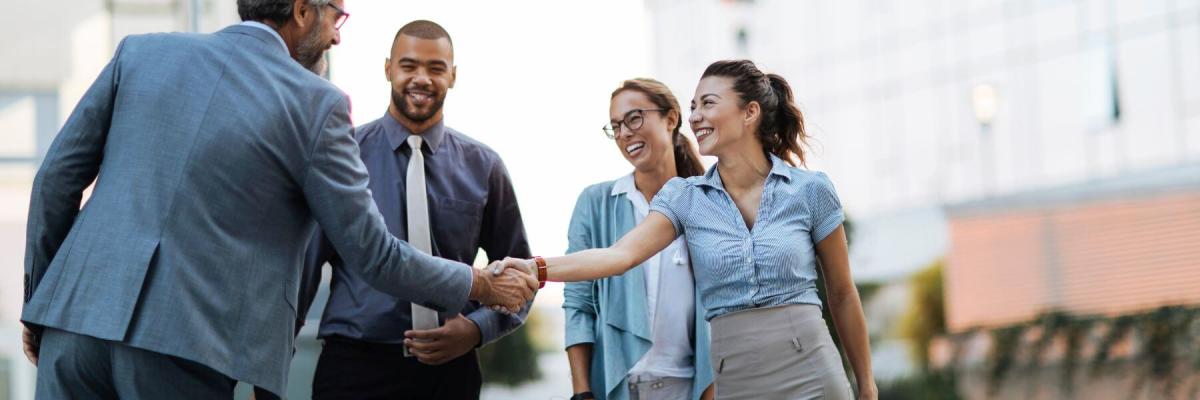 four business people in a circle outside, two shaking hands