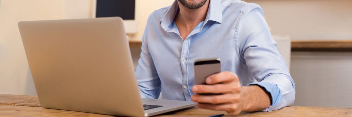 business man printing from mobile phone, sitting at laptop