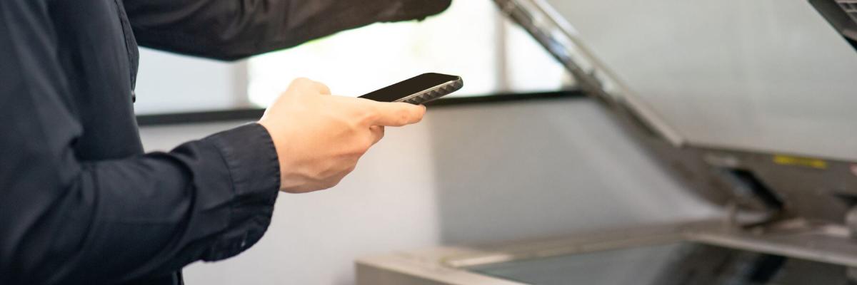 hand holding mobile phone next to open copier